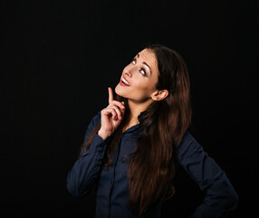 Fototapeta premium Beautiful thinking excited business woman looking up and pointing the finger above in office clothing on black background with empty copy space for text. Closeup