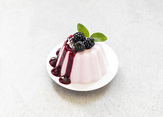 Blackberry cream pudding with sauce, on a plate. Light grey background. Top view