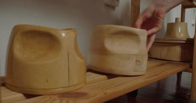 Woman arranges wooden molds for making hats in rows on shelf