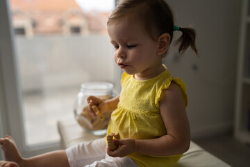 One baby girl sitting at home and eating cookies from glass jar