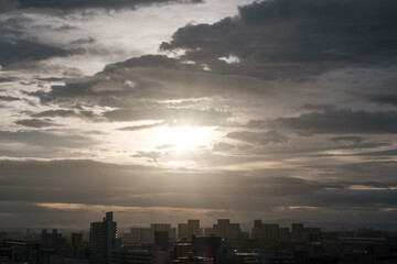 厚い雲に覆われた東の空から太陽が姿を表し。高層ビルがシルエットで浮かび上がる。早朝神戸市内より芦屋大阪方面を臨む。