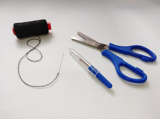 Fabric scissors, seam ripper, black thread, hand sewing needle isolated on a white background.