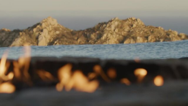 Rack focus from fire pit and infinity pool to Cabo mountains at sunset