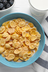 Bowl of tasty corn flakes and blueberries served for breakfast on white wooden table, flat lay