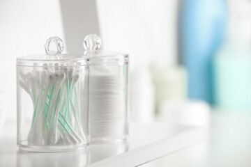 Containers with cotton swabs and pads on white shelf in bathroom, closeup. Space for text