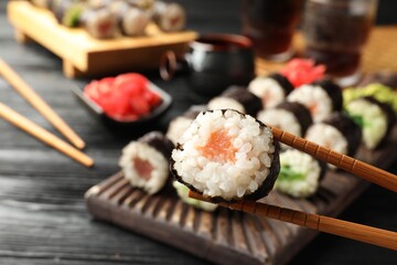 Set of delicious sushi rolls and chopsticks on black wooden table, closeup. Space for text
