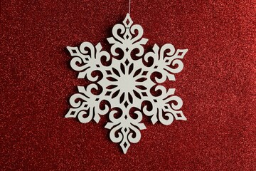 Beautiful decorative snowflake hanging on sparkling red glitter background, closeup