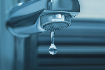 Water drop falling down from tap on blurred background, closeup