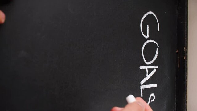 Vertical video of hand writting  goals with white chalk on blackboard 