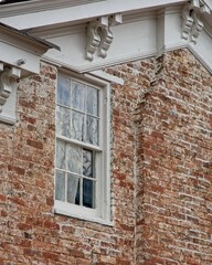 Wooden window set in brick wall under soffit eaves with decorative corbels on antique brick house © JohnBlottman