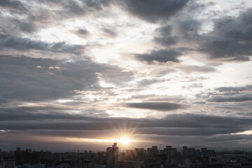 厚い雲に覆われた東の空から太陽が姿を表し。高層ビルがシルエットで浮かび上がる。早朝神戸市内より芦屋大阪方面を臨む。