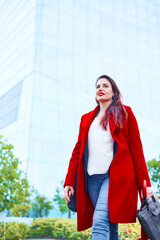 Middle-aged woman walking to a job interview dressed in a white blouse and red coat looking to the side. Defocused background of an office building and the sky. Copy space Business executive woman.