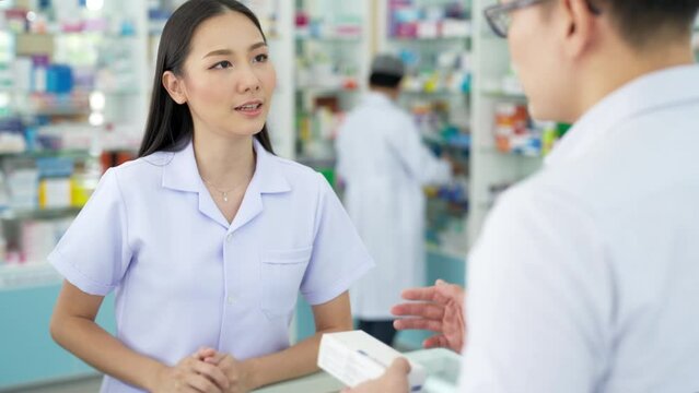 4K Attractive Asian woman pharmacist medication recommendation about medicine, drugs and supplements to male patient customer in modern drugstore. Medical pharmacy and healthcare providers concept.