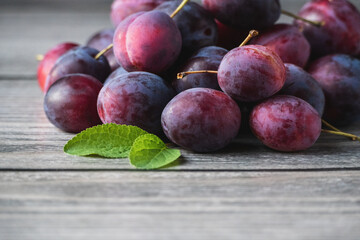 Harvested plums on wooden table, purple prune fruits, green leaf, copy space