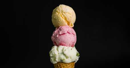 Close-up of an ice cream cone with three flavors together Coconut milk and strawberry vanilla on black background.