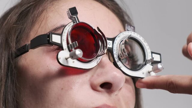 Attentive optometrist examines a beautiful female patient, checks her vision in an ophthalmological clinic. Close-up of a doctor inserting a green-red lens into a trial frame
