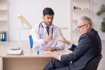 Old businessman visiting young male doctor in vaccination concep