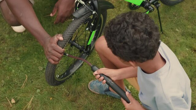 African dad helps his son repair his bike on the lawn near the house.Multiracial Family,Mixed Race,Diverse People,Multiethnic Relations