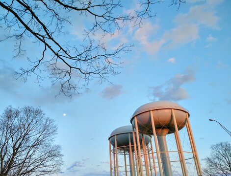 Moon and Bare Tree Branches Next to Water Towers
