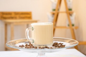 Capuccino en taza de vidrio con granos de cafe y fondo de cafetería