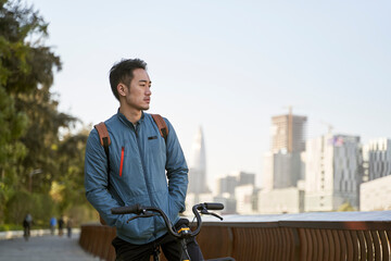 young asian man sitting on his bike lost in thought
