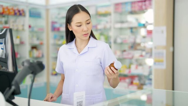 Medical pharmacy and healthcare providers concept. Handsome Asian woman pharmacist working inspection medical product, drugs, medicine and supplements in package at cashier counter in modern drugstore
