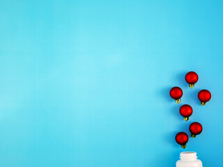 Red Christmas balls like medicine pills blow out or ejection from bottle on blue background. Top view, flat lay, copyspace. Medical banner concept new year or Christmas. Winter holidays in pandemic.