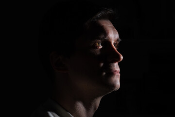 profile of thoughtful man looks to the right. portrait in side light, hard light, photo on black, looks up