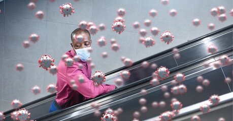 Covid-19 cells against man wearing a face mask using escalator