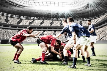Digital composite image of team of rugby players tackling each other to win the ball in sports stadi - obrazy, fototapety, plakaty