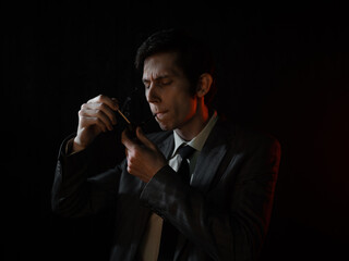 Fototapeta premium A serious young man lights his pipe with a match, a man in a gray suit with a tie, deep shadows in a retro noir style