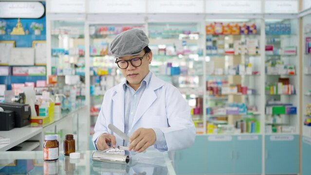 Medical pharmacy and healthcare providers concept. Asian man professional pharmacist counting drug pills on counting trays by hospital prescriptions on counter to patient customer in modern pharmacy.
