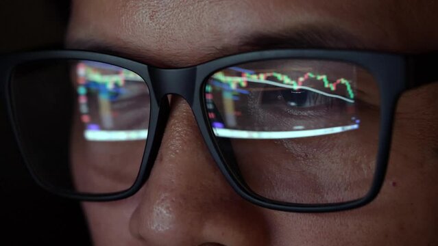 Close-up camera to trader's glasses analyzing stock charts