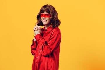 a sweet, happy woman stands in a stylish red shirt and red glasses on a yellow background, smiling broadly and posing in a relaxed pose. Horizontal Studio Photography