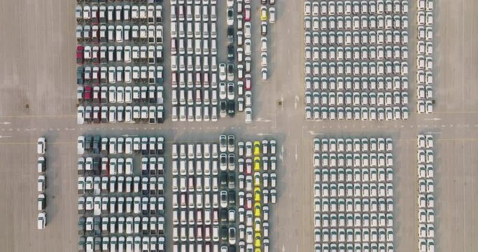 Aerial view of large parking new cars distribution center of modern seaport. Lot of vehicles waiting for sale and transportation shipping by freight cargo vessel ship. Automobile industry.