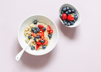 Oatmeal with strawberries, blueberries, nuts and honey on a light background, top view