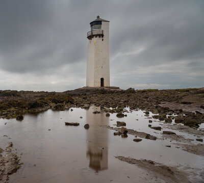 the historic Southerness Lighthouse in Scotland with reflections in tidal pools in the foreground