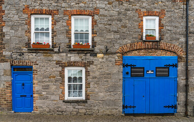 Naklejka premium traditional Irish stone hosue front with brick-framed windows and bright blue doors