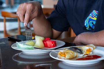 Cropped image of a young casual man eating fresh fruit for breakfast. Fried eggs with sauce and spoon on the dish as a bokeh foreground.