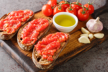 Catalan Pan con Tomate Spanish toasted bread rubbed with fresh garlic and ripe tomato, then drizzled with olive oil closeup on the wooden board on the table. Horizontal - obrazy, fototapety, plakaty