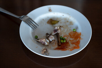 The leftover food and dirty dishes on the restaurant table. Chicken bones, sauce and green beans...