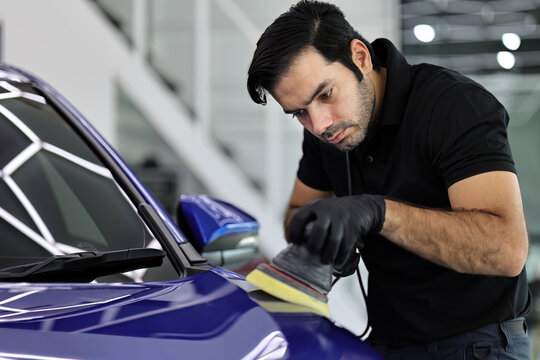 Master polishes the deep blue car via polish mashine in a car workshop.
