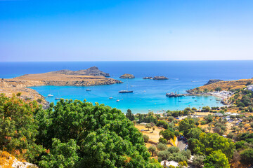 Naklejka na ściany i meble Panoramic view of colorful harbor in Lindos village, Rhodes. Aerial view of beautiful landscape, sea with sailboats and coastline of island of Rhodes in Aegean Sea. High quality photo