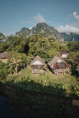 bungalows on the banks of the Nam Xong river on a sunny day with karst mountains in the background in rainy season