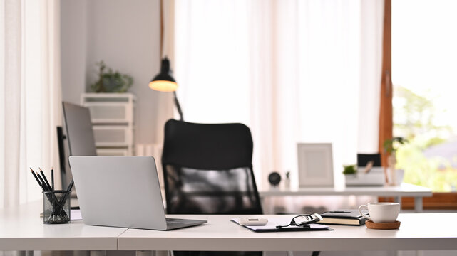 Horizontal image of laptop computer, documents and various office supplies on white table in modern interior