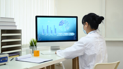 Back view of female scientist working on personal computer with screen showing analysis software in...