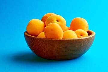 Bright ripe apricots in a wooden bowl on a blue background