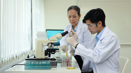 Fototapeta premium Young man researcher and senior supervisor are conducting experiment with test tubes and microscope slides in research laboratory