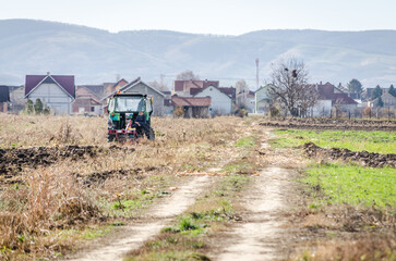 Winter agricultural landscape. Winter plowing arable land with green tractor.