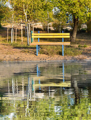Fototapeta premium One yellow bench in the autumn park is reflected in the water. Beautiful autumn background. Loneliness concept.
